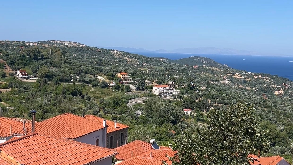 Αμφιθεατρική άποψη της Κύμης Εύβοιας με κόκκινες κεραμοσκεπές, πράσινη βλάστηση και θέα στο Αιγαίο πέλαγος